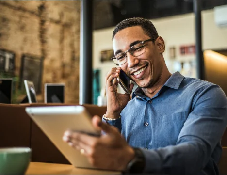 A person speaks on a phone while looking at a tablet